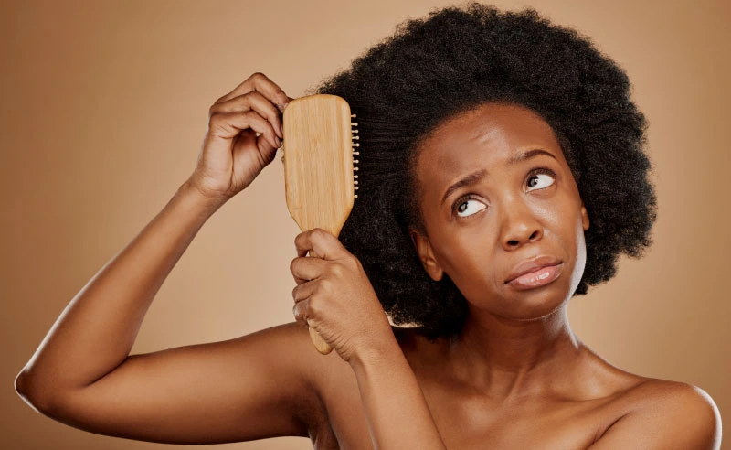 A black woman looking concerned while examining her hair, highlighting hair loss and scalp health issues.