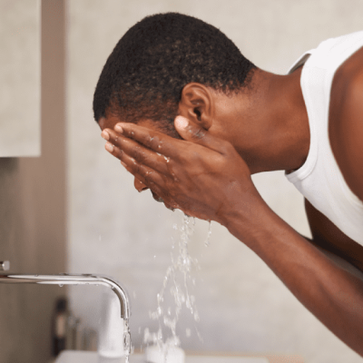 A young man washing his face with water to prevent acne breakouts, illustrating skin care routines in Kampala.
